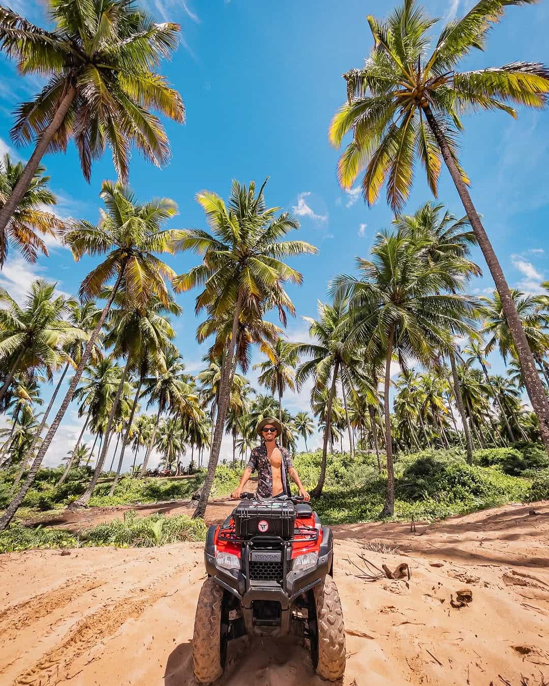 Viajante em um quadriciclo vermelho entre os coqueirais da Península de Maraú